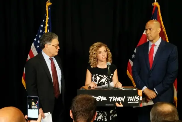 Wasserman Schultz, center, standing in front of a podium providing an incredible self-own
